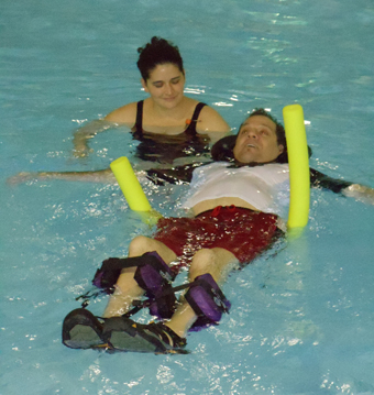 Individual with spinal cord injury floats in pool with an able-bodied assitant.