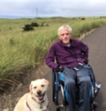 Lan Remme seated in a wheelchair, outdoors, with a dog sitting at his feet